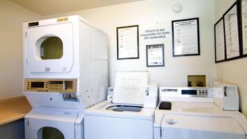 A laundry room with multiple washing machines and dryers, a wall-mounted sign, and several framed documents.