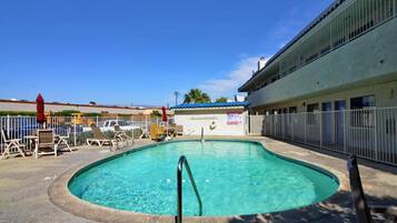 A swimming pool with a metal ladder, surrounded by a fence, and a building with a blue roof in the background.