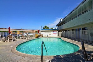 Ein Swimmingpool mit einer Metallleiter, umgeben von einem Zaun, und ein Gebäude mit blauem Dach im Hintergrund.
