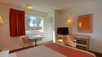 A hotel room with a bed, a desk, a chair, a television, and a window with curtains.
