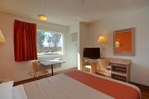Quarto de hotel com cama, escrivaninha, cadeira, televisão e janela com cortinas.