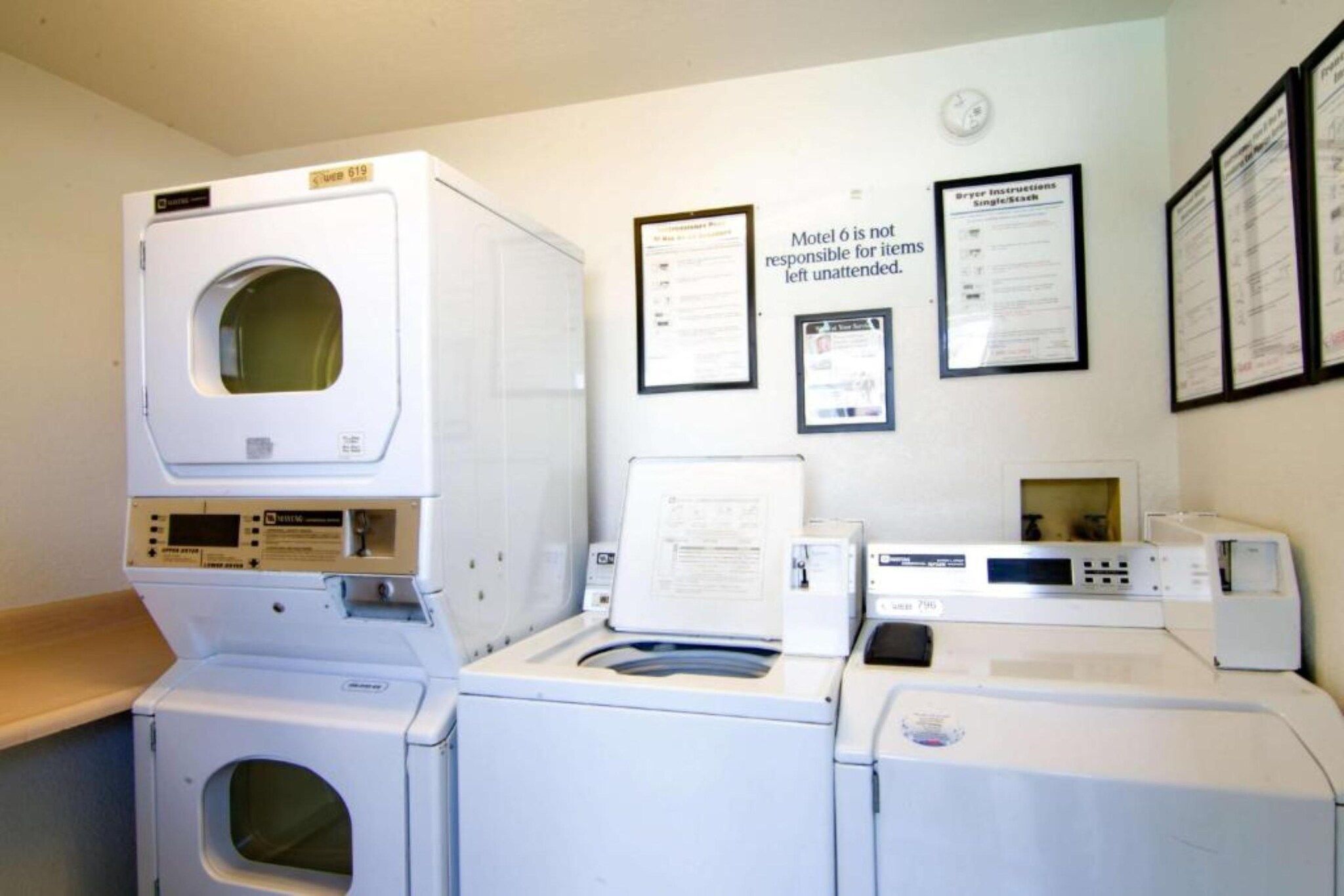 Une buanderie équipée de plusieurs machines à laver et de plusieurs sèche-linge, avec un panneau fixé au mur et plusieurs documents encadrés.