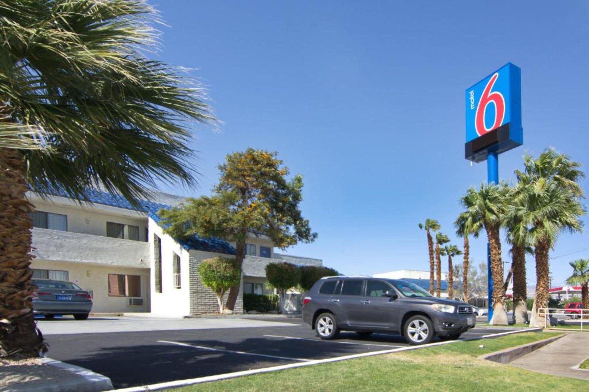 Un motel avec une grande enseigne bleue, des voitures garées et des palmiers.