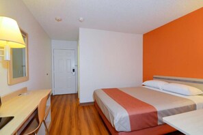 A hotel room with a bed, a desk, a chair, and a lamp.