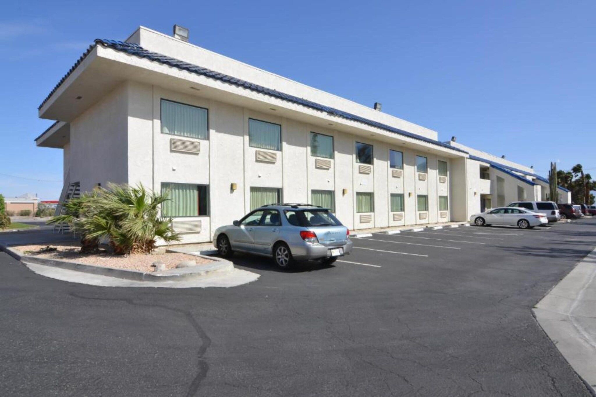 Um motel com uma fileira de quartos, um estacionamento e um único carro estacionado na frente.