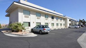 Um motel com uma fileira de quartos, um estacionamento e um único carro estacionado na frente.