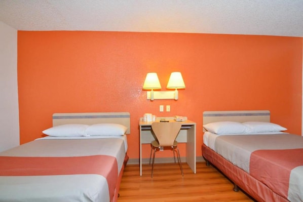 A hotel room with two beds, a desk, and two lamps.