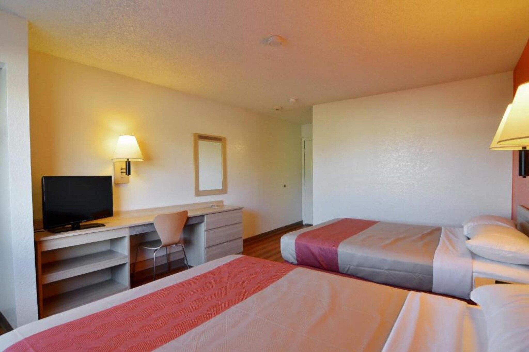 Quarto de hotel com duas camas, uma escrivaninha, uma cadeira e uma televisão.