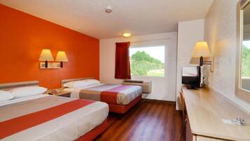 Een hotelkamer met twee bedden, een bureau, een televisie en een raam met uitzicht op groen.