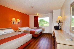 Habitación de hotel con dos camas, un escritorio, un televisor y una ventana con vistas a la vegetación.