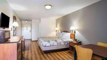 Quarto de hotel com cama, escrivaninha, cadeira, televisão e luminárias.