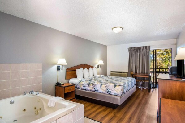 Une chambre d’hôtel avec un grand lit, une salle de bain séparée avec une baignoire, un bureau avec une chaise et un téléviseur.