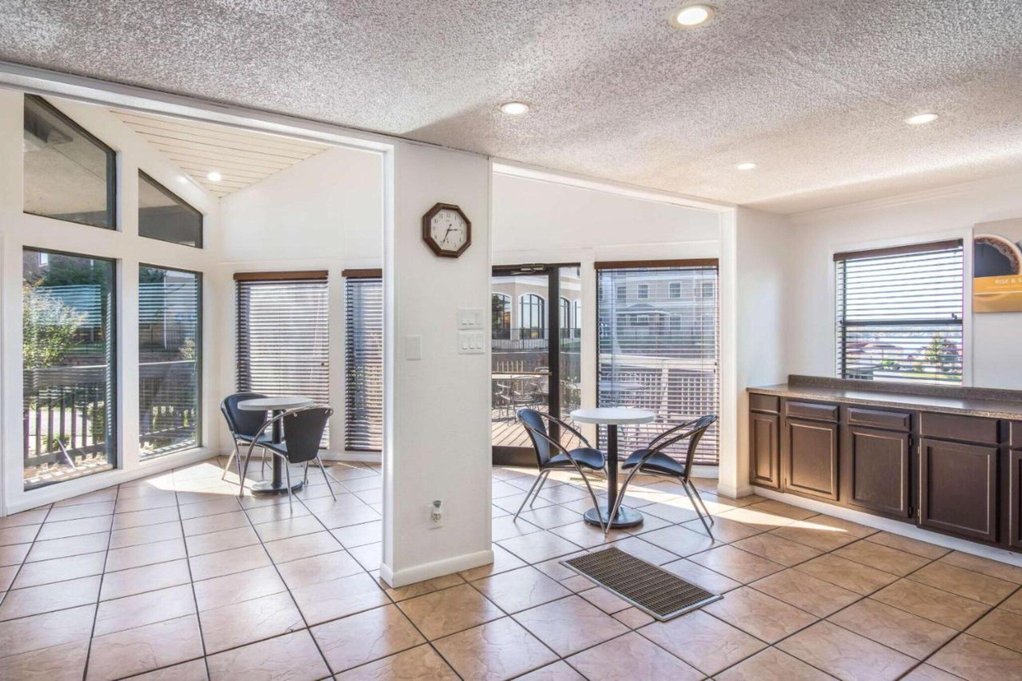 A modern kitchen with dark cabinets, a dining area with a table and chairs, and large windows with blinds.