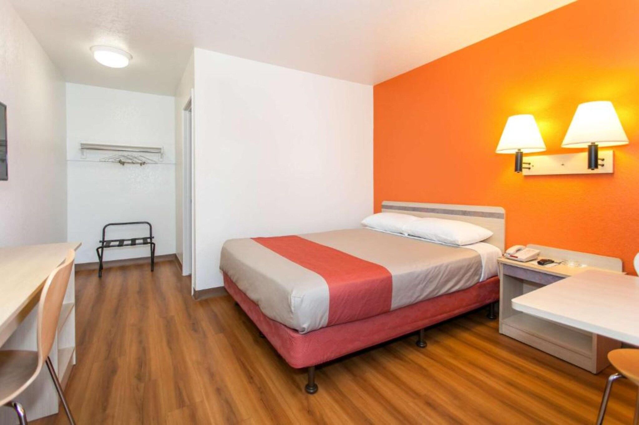 A hotel room with a bed, bedside table, lamp, chair, and a desk.