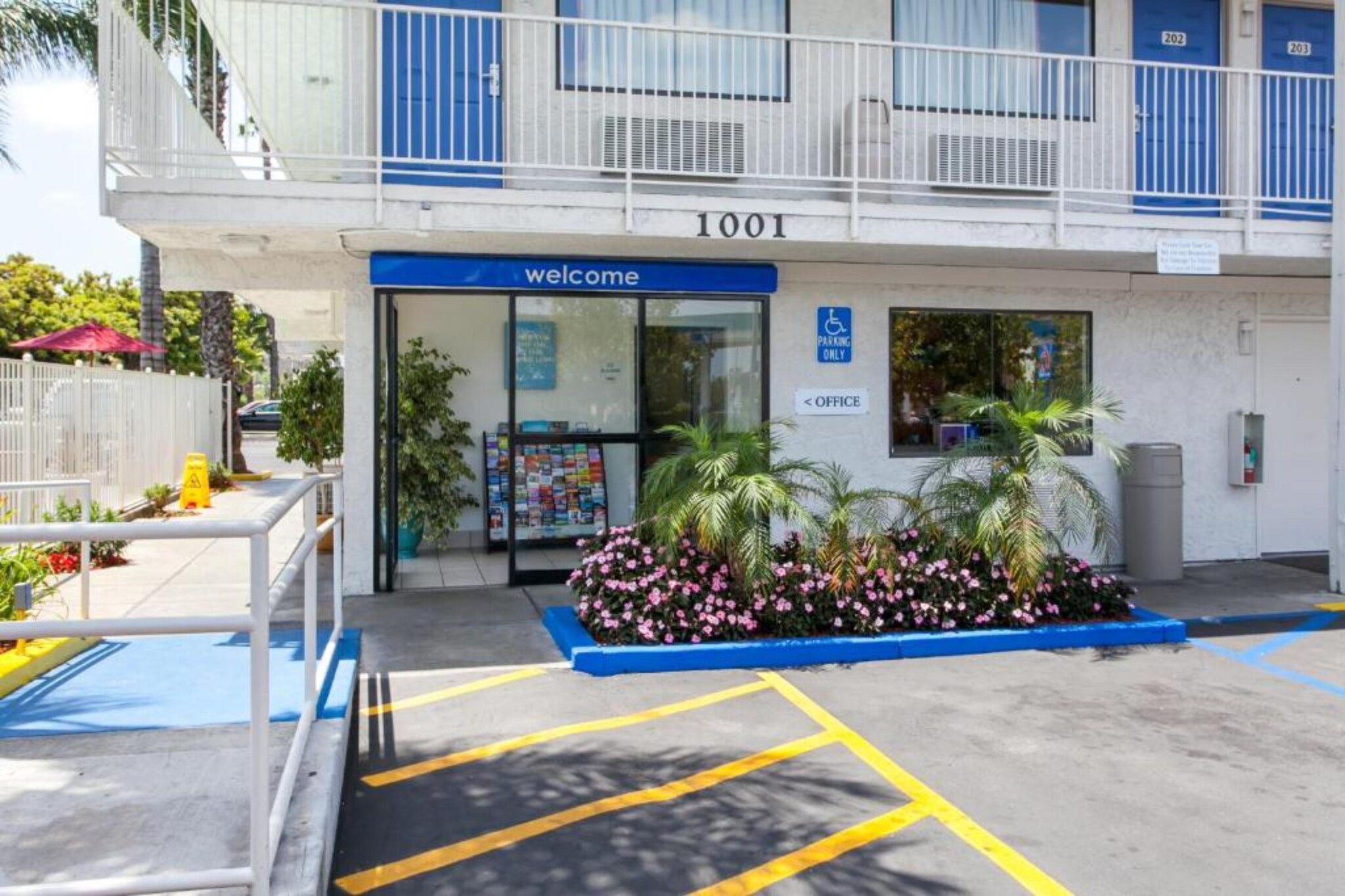 A building with a blue entrance, a welcome sign, and a parking sign indicating a disabled parking space.