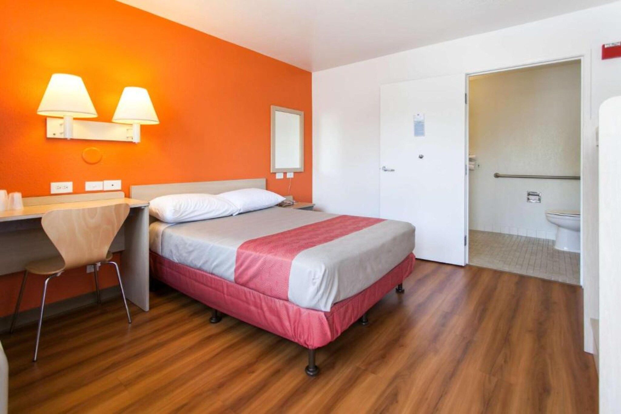 A hotel room with a bed, a desk with a chair, a bathroom, and a door.