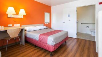 A hotel room with a bed, a desk with a chair, a bathroom, and a door.