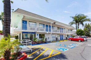 Een meerlaags motel met een parkeerplaats, daarop aangeduide parkeerplaatsen voor gehandicapten en een zichtbare ingang.