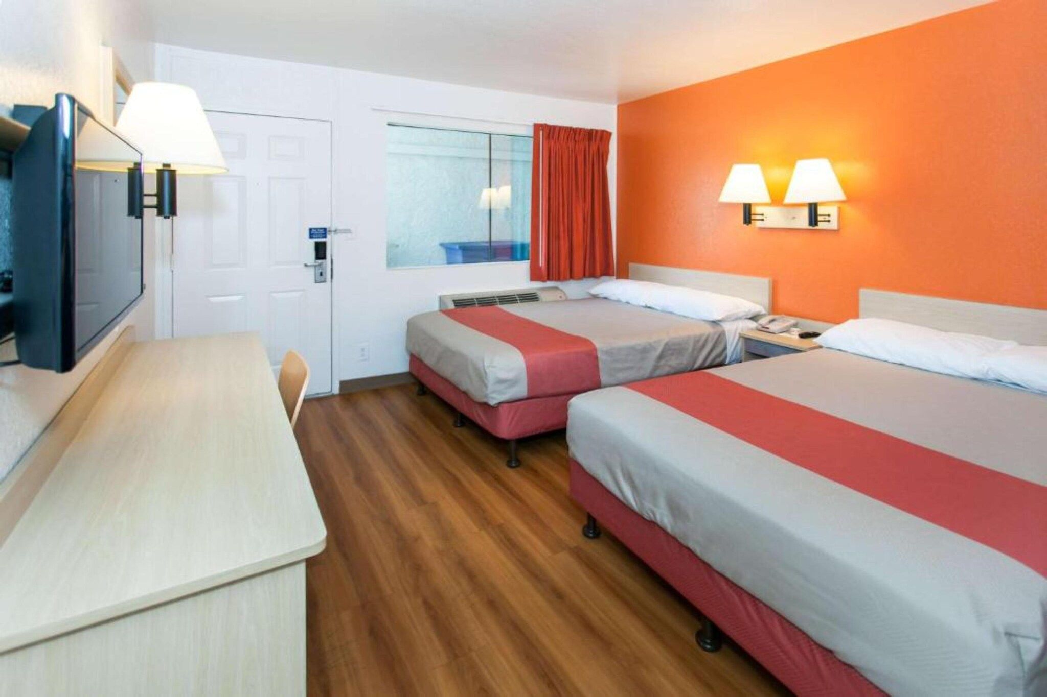 A hotel room with two beds, a desk, a chair, a television, and a window with curtains.