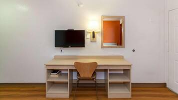 A room with a wooden desk, a chair, a television mounted on the wall, and a mirror.