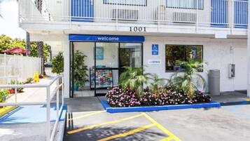 A building entrance with a 'Welcome' sign, a parking sign, and a blue awning.