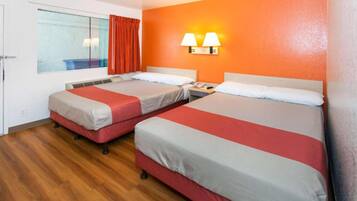 A hotel room with two beds, a window with curtains, a wall-mounted lamp, and a wooden floor.