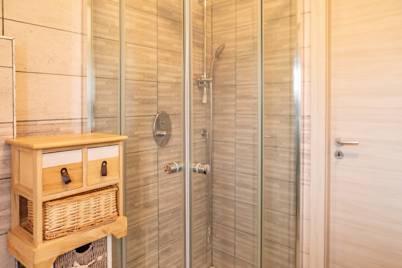 Eine Eckdusche mit Glastür, ein Holzkabinet mit Schubladen und ein Korbwannenweidenkorb.
