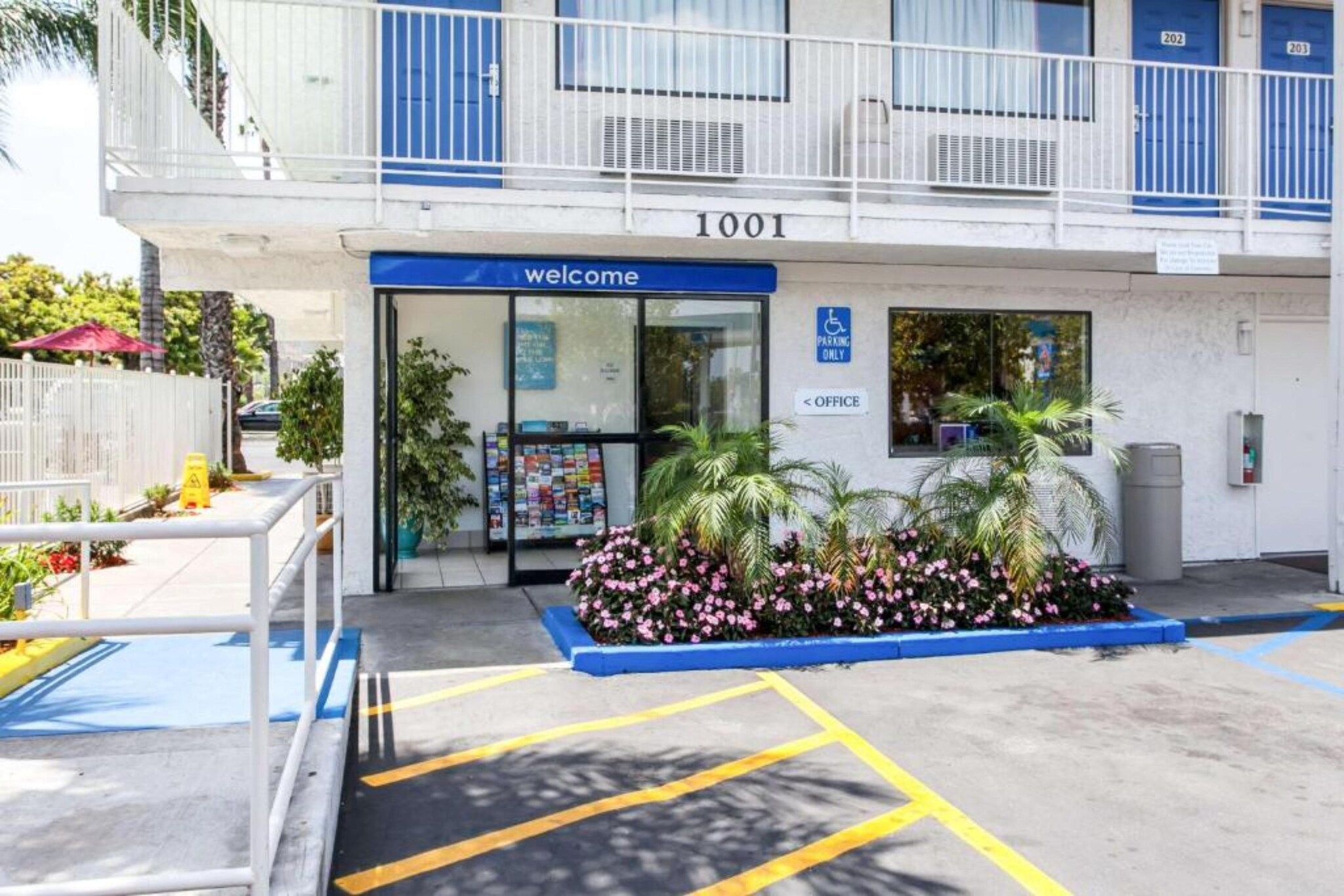 A building entrance with a 'Welcome' sign, a parking sign, and a blue awning.