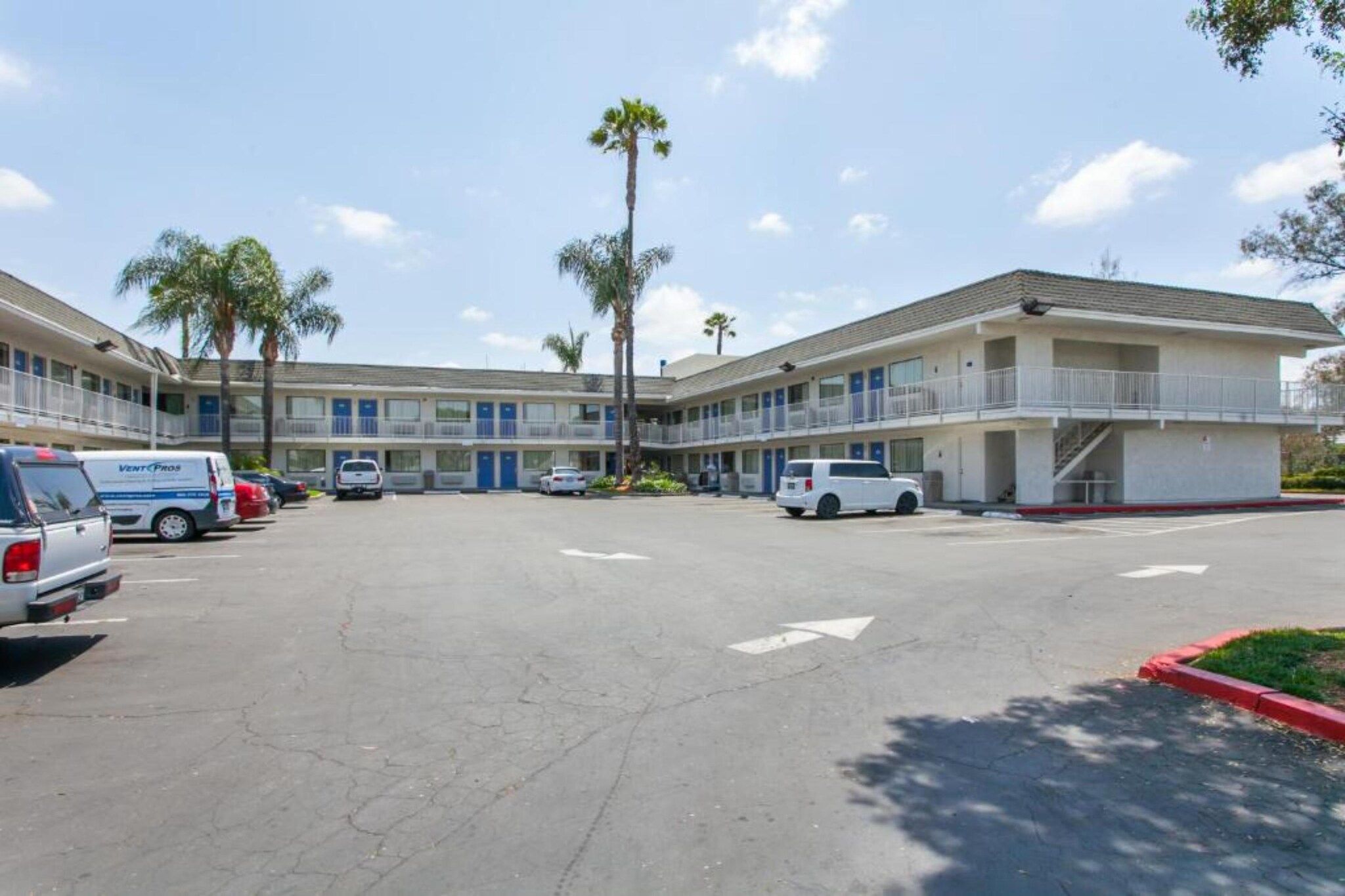 A motel with multiple rooms, a parking lot, and a few parked vehicles.
