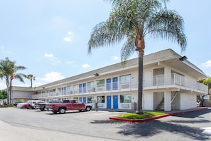 A motel with a two-story structure, a parking lot with several vehicles, and a palm tree in front. - 2 Full Beds | Mini Fridge (Rosemead)