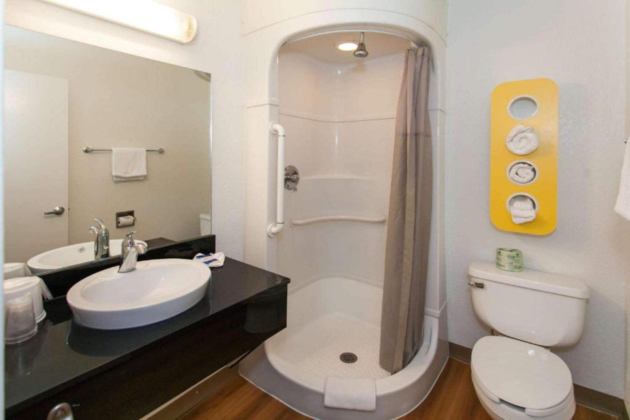 A bathroom with a sink, mirror, shower, toilet, and a towel rack.