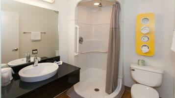 A bathroom with a sink, mirror, shower, toilet, and a towel rack.