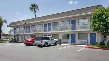 A motel with a two-story structure, a parking lot, and a palm tree.