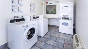A laundry facility with a front-loading washer and dryer, a small window with a plant, and informational posters on the wall.