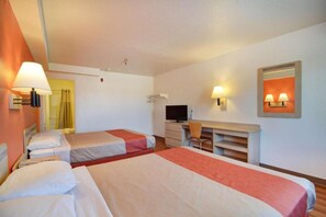 Ein Hotelzimmer mit zwei Betten, einem Schreibtisch, einem Fernseher und einem Spiegel.