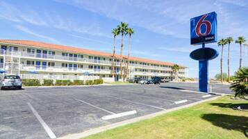 Ein Motel mit großem Parkplatz, mehreren Stockwerken und Palmen.
