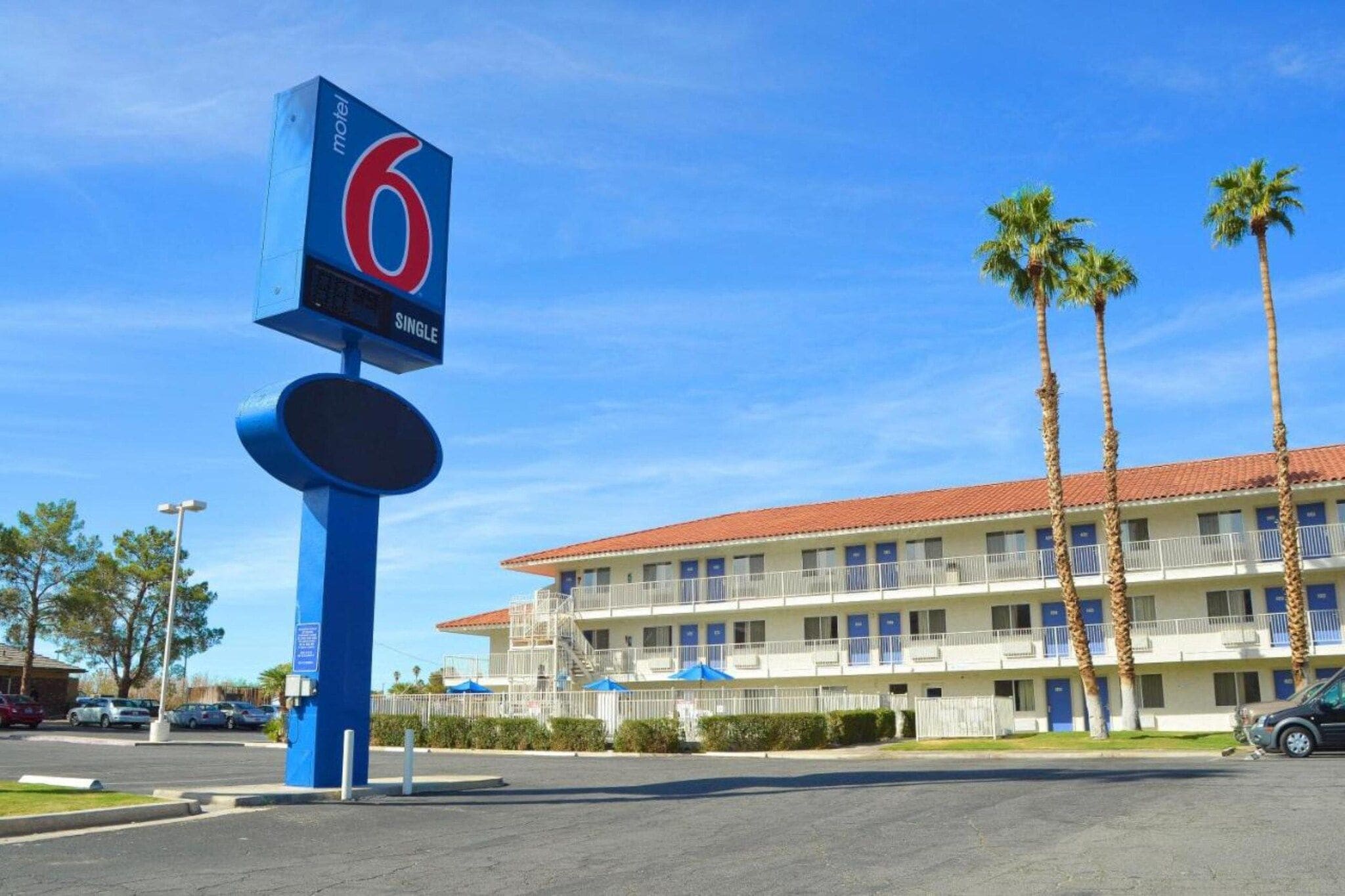 Um motel com uma placa chamativa, estacionamento e um prédio com telhado de telhas vermelhas.