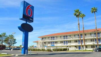 Um motel com uma placa chamativa, estacionamento e um prédio com telhado de telhas vermelhas.