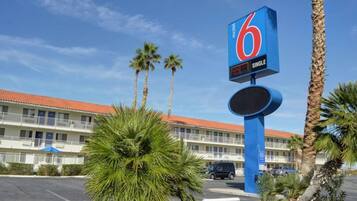 A motel with a prominent '6' sign, a parking lot, and palm trees.