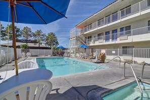 Una piscina con valla blanca, una sombrilla azul y un edificio con balcones al fondo.