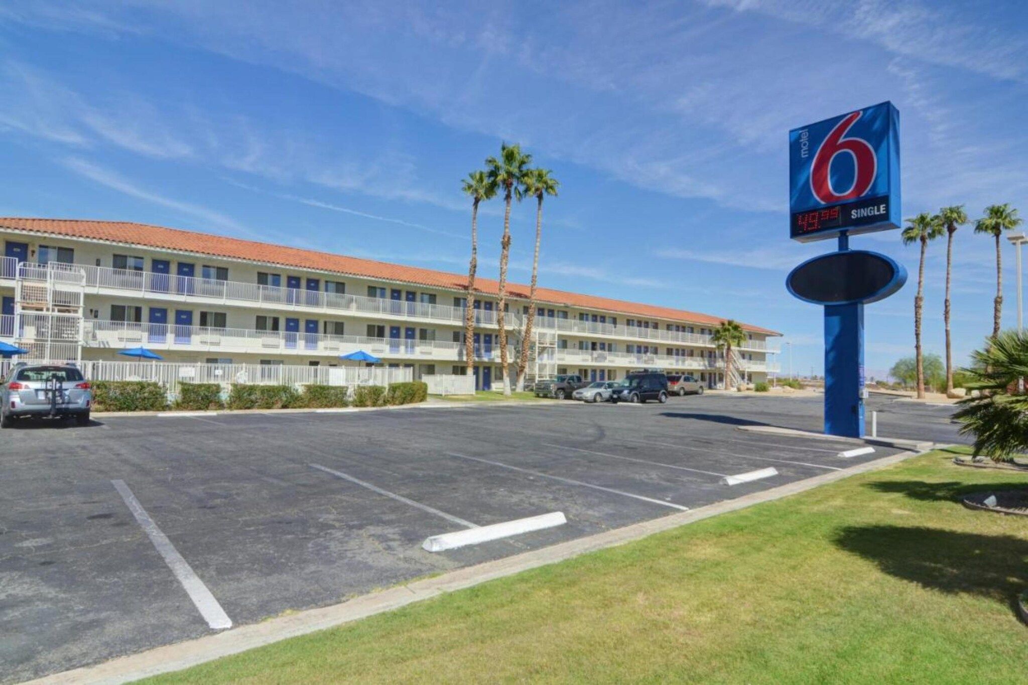 Un motel con estacionamiento, edificios de varios pisos y palmeras.