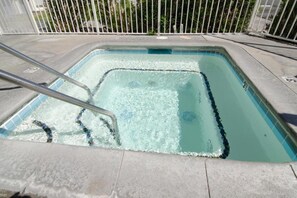 Ein rechteckiger Pool mit einer Metallleiter, umgeben von einer Betonplattform und einem weißen Zaun.