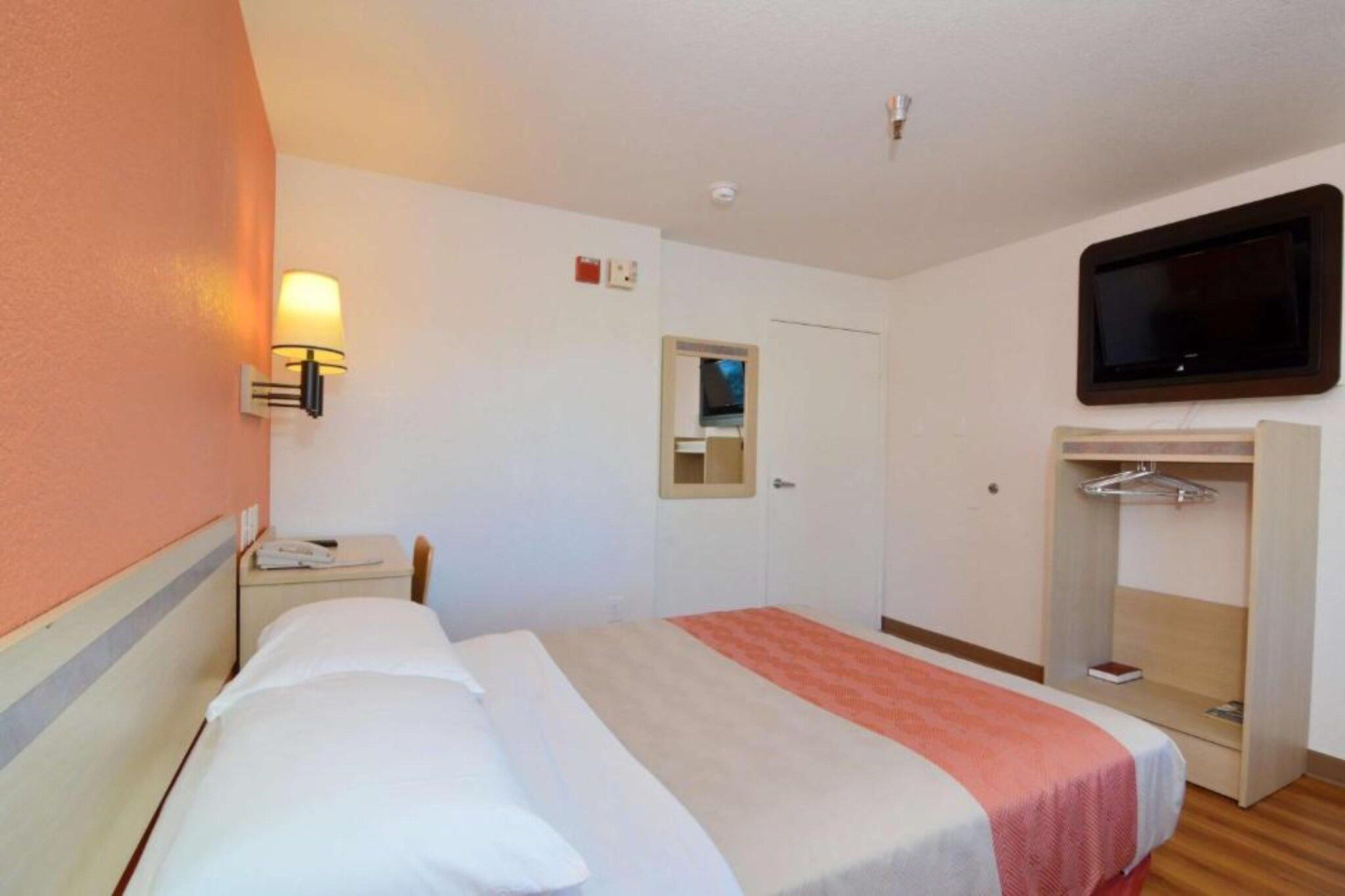 A hotel room with a bed, a bedside table, a TV mounted on the wall, a wardrobe, and a mirror.