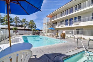 Una piscina con una cerca blanca, una mesa con sillas y un edificio con balcones.