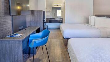 Ein Hotelzimmer mit Schreibtisch, blauem Sessel, zwei Betten und einem durchgegangenen Tür erkennbaren Badezimmer.