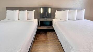 A hotel room with two beds, a nightstand with a lamp, and a wooden floor.