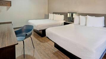 A hotel room with two beds, a desk, a chair, and a bedside table.