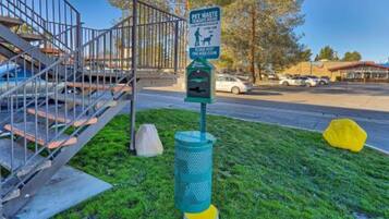 Una estación de manejo de residuos de mascotas, con un bote de basura y un letrero, ubicada cerca de una escalera y un estacionamiento.