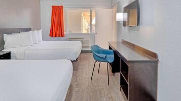 Ein Hotelzimmer mit zwei Betten, einem Schreibtisch, einem Stuhl, einem fenster mit Vorhängen und einem Spiegel an der Wand.