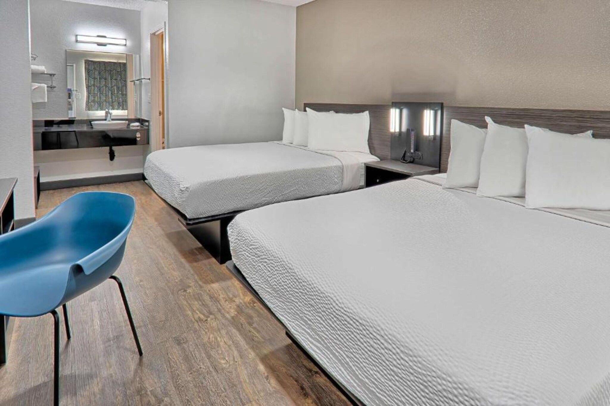 A hotel room with two beds, a desk, a chair, and a television.